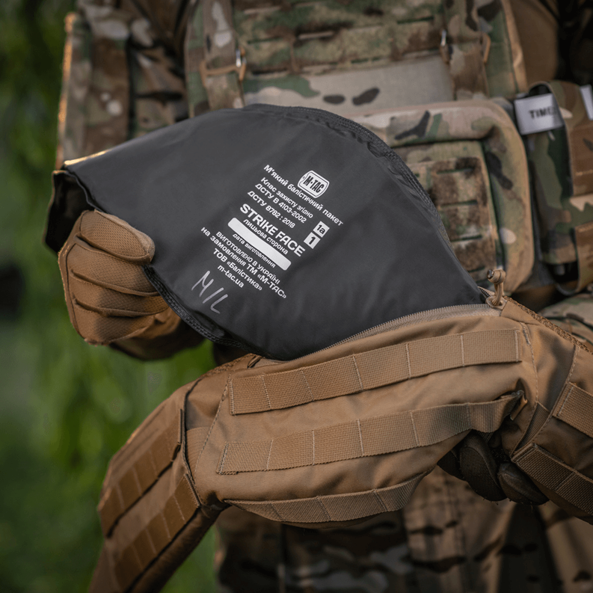 War Belt ARMOR holdt af taktisk udstyret person med camo-vest og MOLLE-stropper, fremhæver M-Tac produktets holdbarhed og funktionalitet.