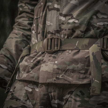 Close-up of a military uniform with camouflage pattern, focusing on the belt area in a woodland environment.