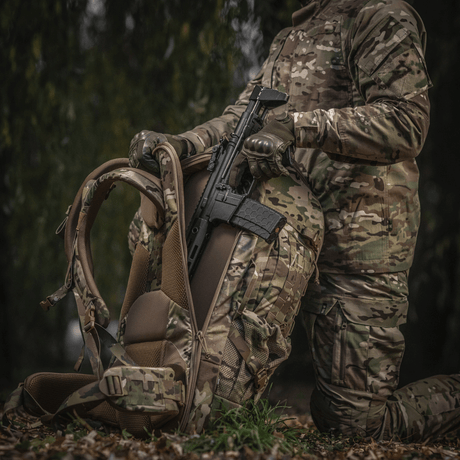 Person in camouflage holding a weapon and M-Tac Large Gen.IV Elite backpack in a forest area.