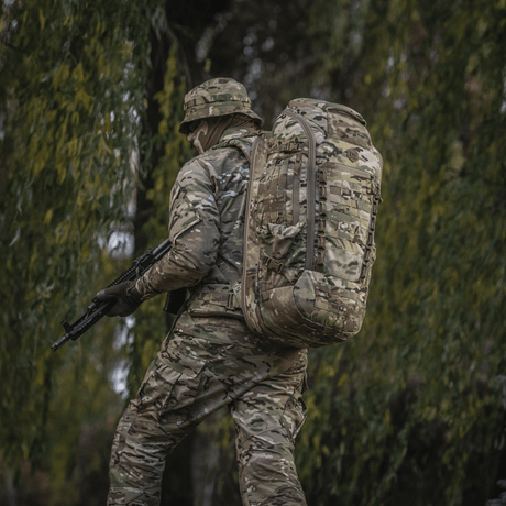 Soldier with camouflaged M-Tac Large Gen.IV Elite backpack in a woodland environment.