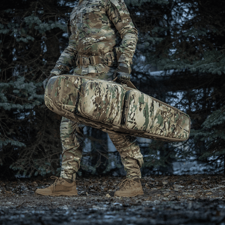 Soldier carrying M-Tac Gun Backpack Case 125 cm Gen.II Elite in a forest, wearing camouflage uniform