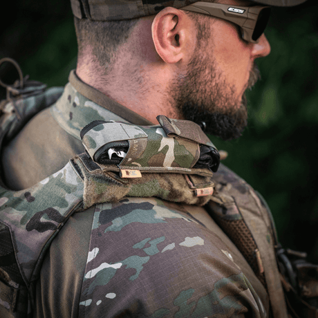 M-Tac Tourniquet Pouch Elastisk med MOLLE Gen.II på skulder af en taktisk klædt mand udendørs, hurtig adgang sikkerhed.