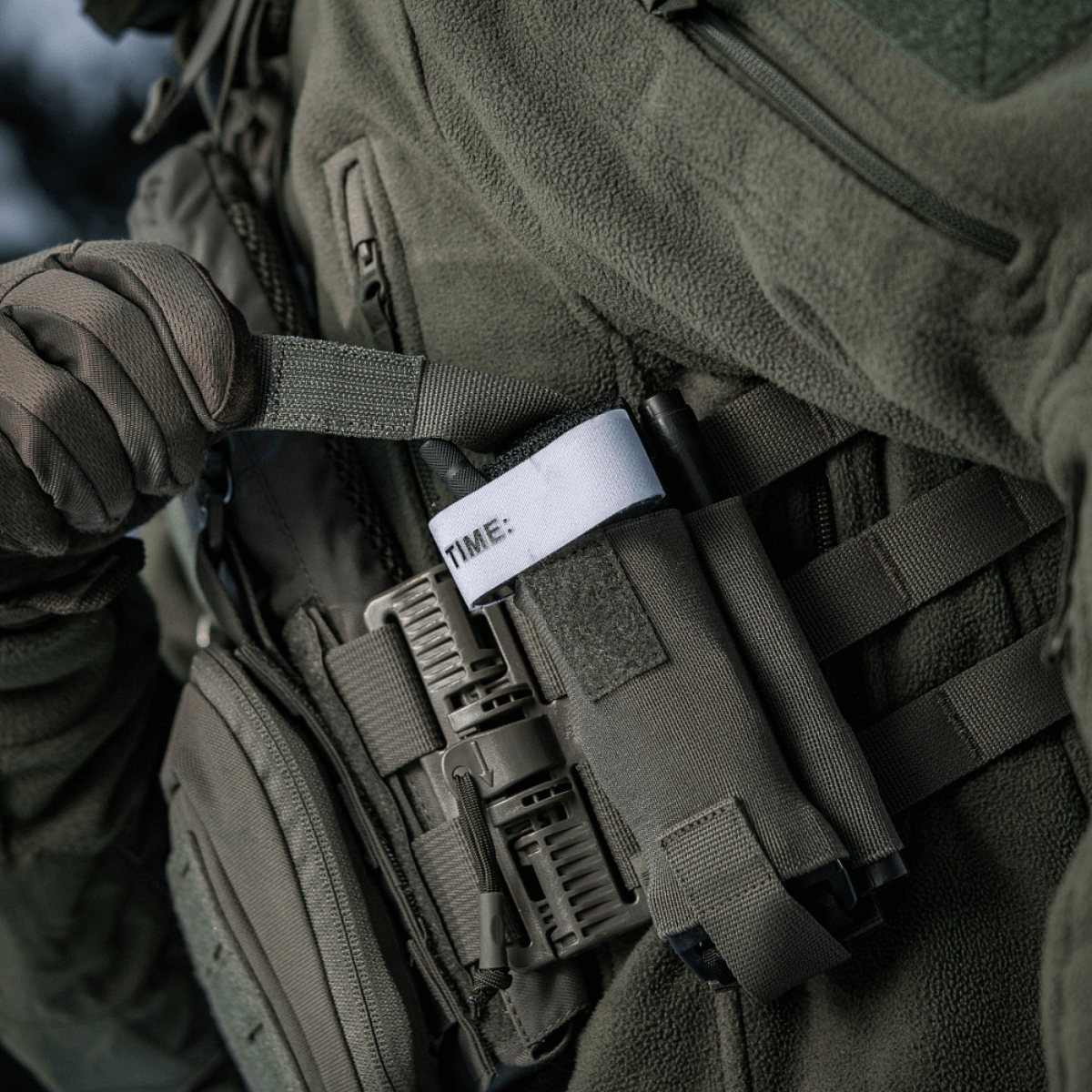 M-Tac Elastisk Tourniquet Pouch Molle Gen.III fastgjort til en taktisk vest, der viser praktisk brug med nem adgang til tourniquet.