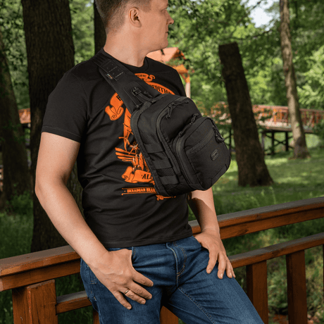 Man wearing M‑Tac Cross Bag Elite Hex sling pack on a bridge in a forest, holds up to 5 L