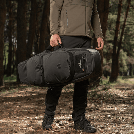 Man carrying M-Tac Gun Backpack Case 105 cm Elite Hex in the woods, ideal for hunting and shooting, designed for AR-15 and AK carbines.