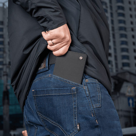 Person puts M‑Tac Pung Slim Elite in back pocket of jeans, compact and stylish design for cards and cash.