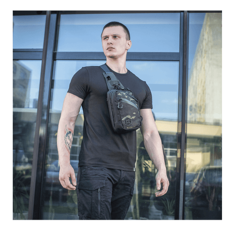 Man wearing M-Tac Sling Pistol Bag Elite Hex in front of a glass building, showing versatility and style.