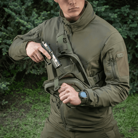 Person with M-Tac Sling Pistol Bag Elite Hex carrying a pistol against a wooded background.