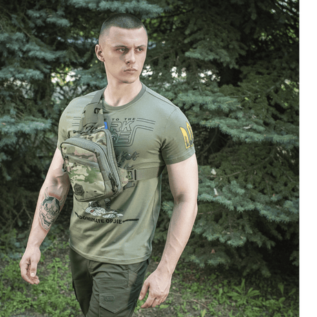Man with green M-Tac Sling Pistol Bag Elite Hex, made from robust Cordura, with adjustable strap in a forest area.