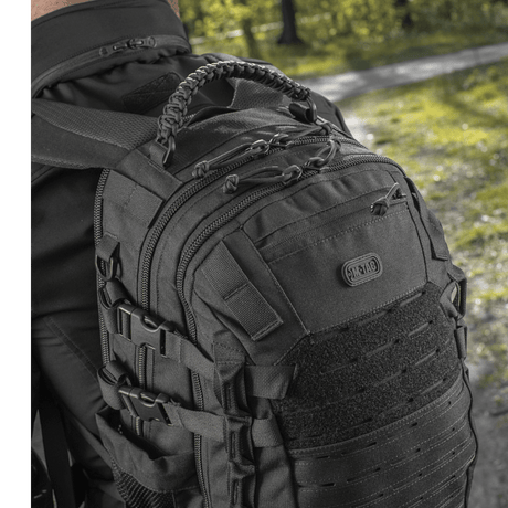 Man wearing M-Tac Mission Pack Elite backpack with ergonomic design and MOLLE LASER CUT system in a forest setting.
