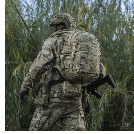 Soldier with M-Tac Mission Pack Elite backpack in camouflage, in a natural environment.