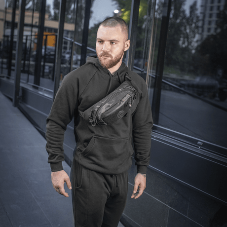 Man wearing M‑Tac Elite Hex belt bag with black clothing outdoors. Compact and stylish bag ideal for everyday use and tactical gear.