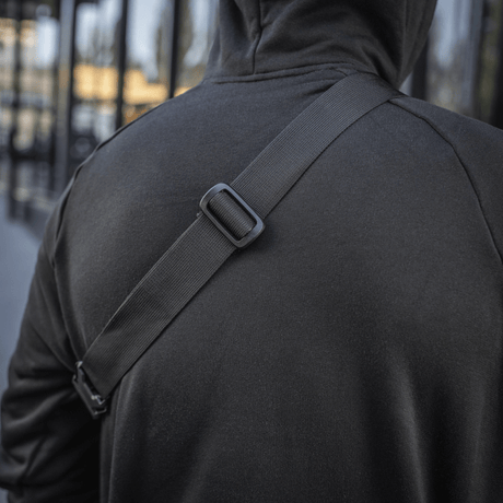 Person in black hoodie wearing M‑Tac Elite Hex belt bag across the shoulder in an everyday setting.