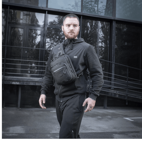 Man with M-Tac Cross Bag Slim Elite Hex wearing black clothing in front of a modern building.