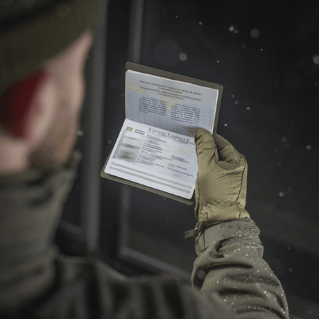 Person holding a passport protected by an M‑Tac passport cover while wearing winter clothing.