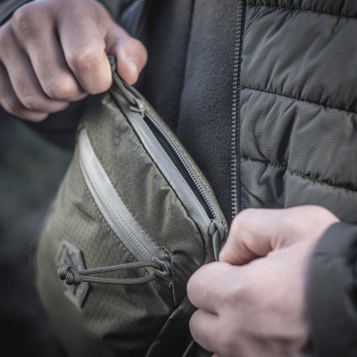 M‑Tac Pocket Bag Elite HEX med holdbare YKK lynlåse vises som kompakt taske i brug, perfekt til opbevaring af småting og udstyr.