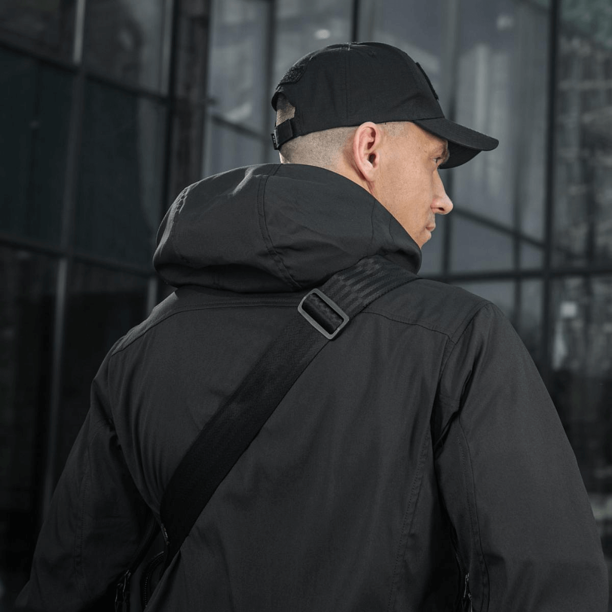 Person carrying M-Tac Tablet Bag Laser Cut Hex over the shoulder with black jacket and cap, urban background.