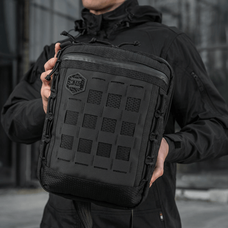 Mand holder en M-Tac Tablet Bag Laser Cut Hex i hånden, lavet af Cordura materialer med Laser Cut MOLLE panel på forsiden.