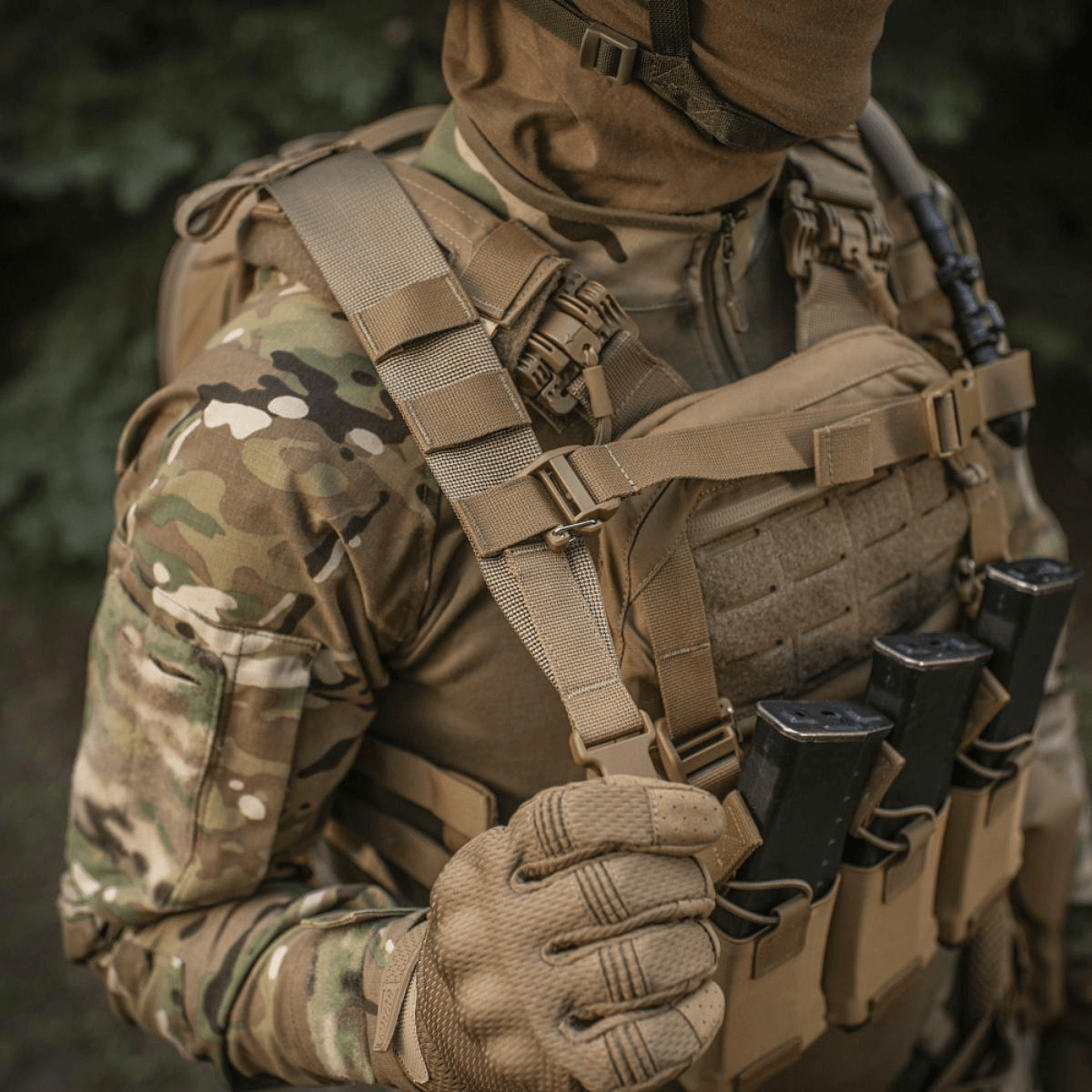 Soldat i camouflageuniform med taktisk vest og magasiner udendørs, set tæt på.