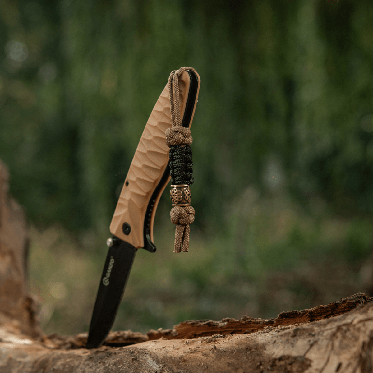 M-Tac Lanyard Scandinavian Small Chinese Knot attached to a knife handle on a tree stump in a forest setting.