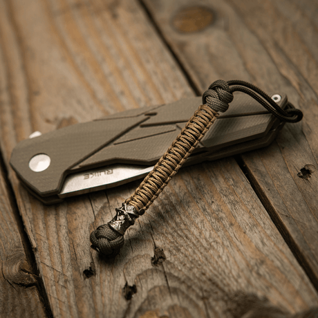 M-Tac Knife Lanyard Ninja in paracord beside folding knife on wooden table