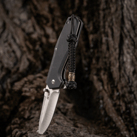 M-Tac Knife Lanyard Celtic in braided paracord mounted on a knife against a rustic background.