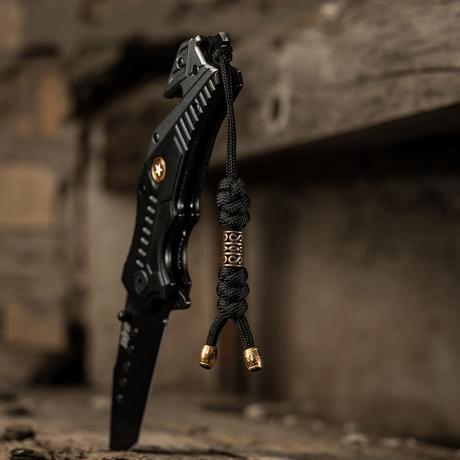 M-Tac Zeus Lanyard in braided paracord tied to black knife on a rustic surface, flexible accessory for quick access to gear.