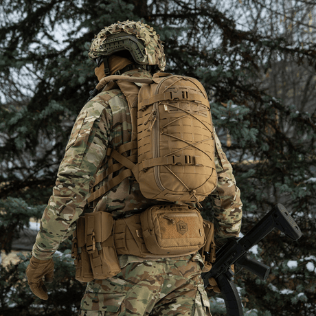 M-Tac Sturm Elite Gen.II backpack in the field, person in camouflage wearing tactical backpack with MOLLE system and reinforced straps, forest setting.