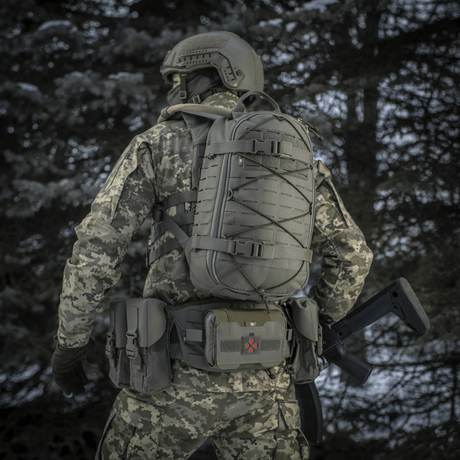 Tactical person with M-Tac Sturm Elite Gen.II backpack in a forest environment wearing camouflage uniform, rear view.