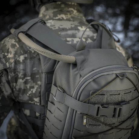 M-Tac Sturm Elite Gen.II in gray Cordura on a soldier wearing camouflage, showing built-in hydration system with tube in an outdoor setting.