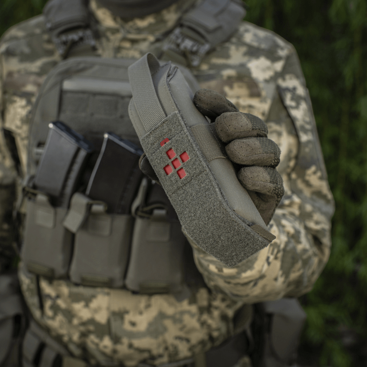 En soldat holder M-Tac Lomme til Tourniquet Closed i naturen, designet til pålidelig beskyttelse i nødsituationer.