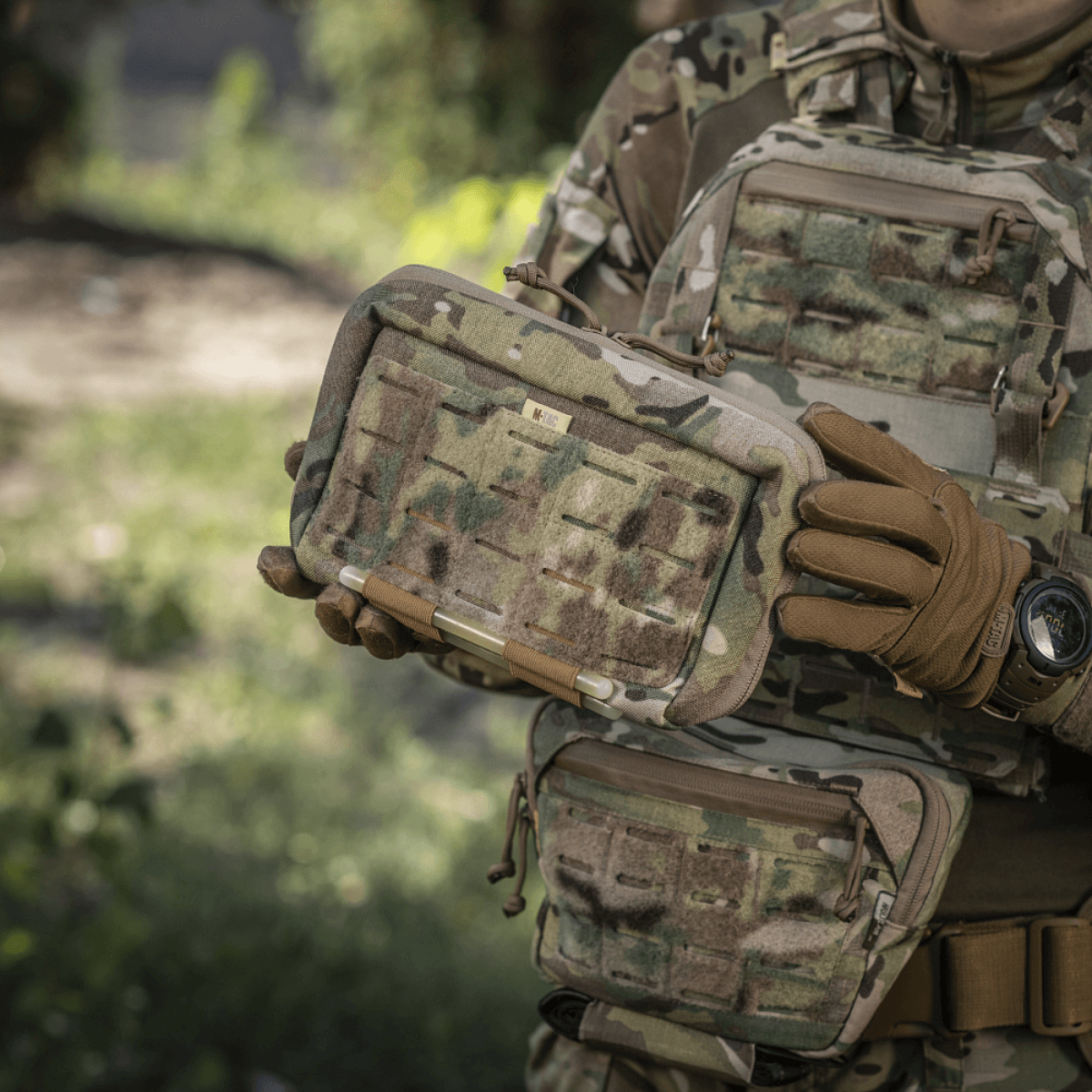 M-Tac Admin Pouch Large Elite bliver holdt af person iført camouflagedragt, ideel til opbevaring af taktisk udstyr i felten.