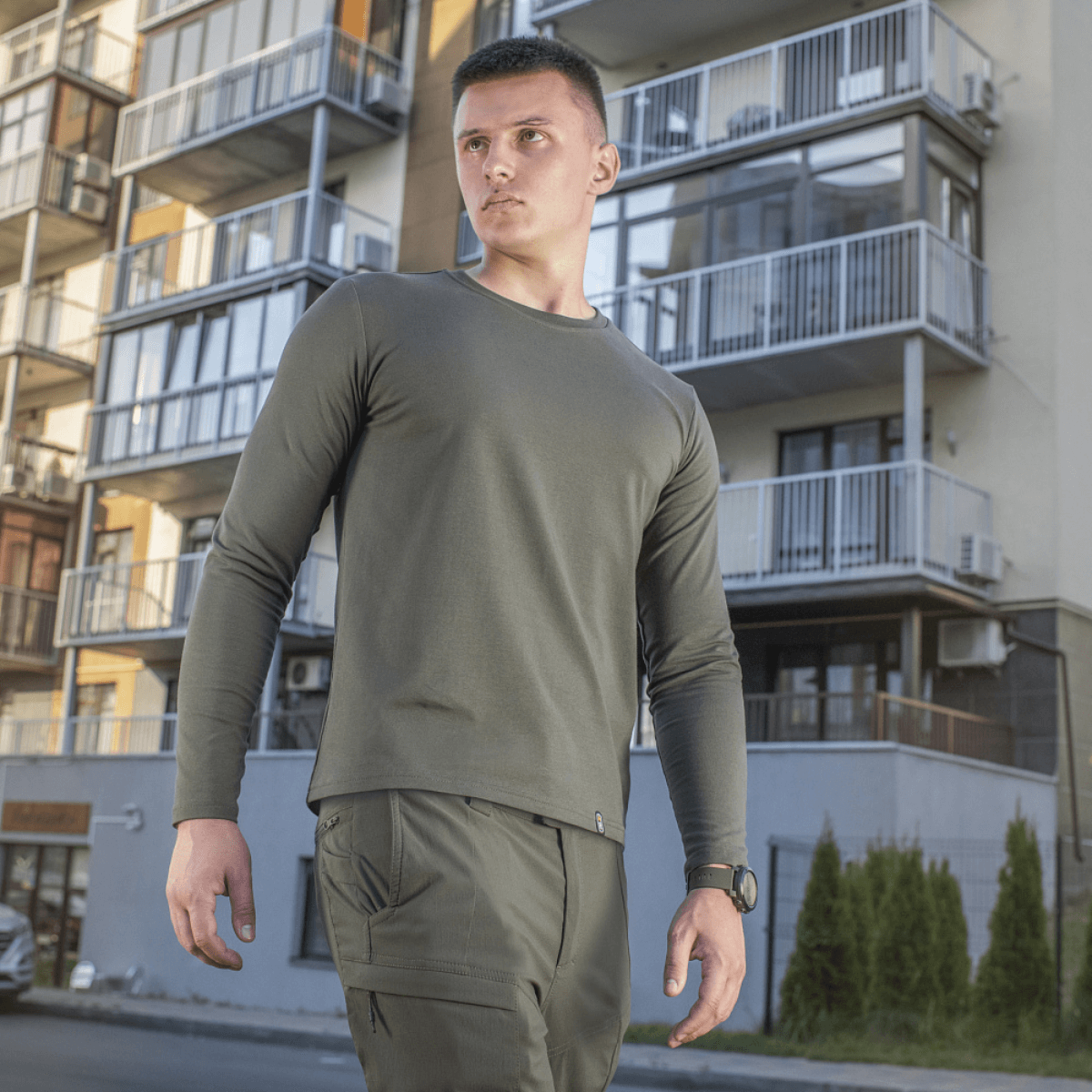 Mand iført M-Tac Long-sleeve T-shirt 93/7 foran moderne bygninger, perfekt til hverdag, uniformer og friluftsliv.