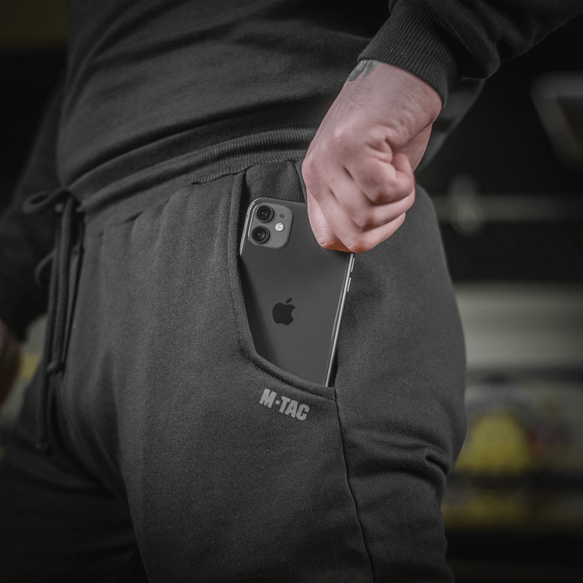 Mand iført M-Tac Bukser Cotton Classic, viser en smartphone i buksernes sidelomme, som er perfekt til sport og daglig brug.
