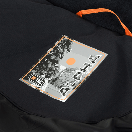 Label på M-Tac Alpha Gen.III Pro Vinterjakke, der viser logo og design af mærket. Vinterjakke kombinerer stil og funktionalitet.