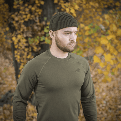 Man wearing M-Tac Raglan Athlete sweatshirt in olive in an autumn landscape, highlighting the raglan sleeves' flexibility and minimalist design.