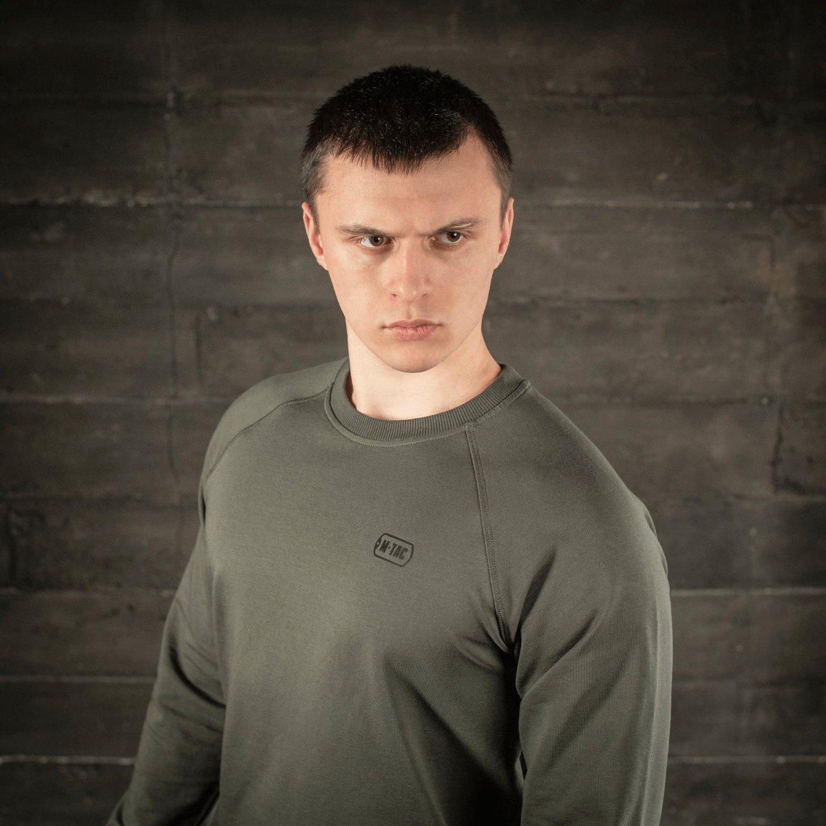 Mand i M-Tac Raglan Athlete sweatshirt i olivenfarve, viser alsidighed og minimalistisk design med raglanærmer for bevægelsesfrihed.