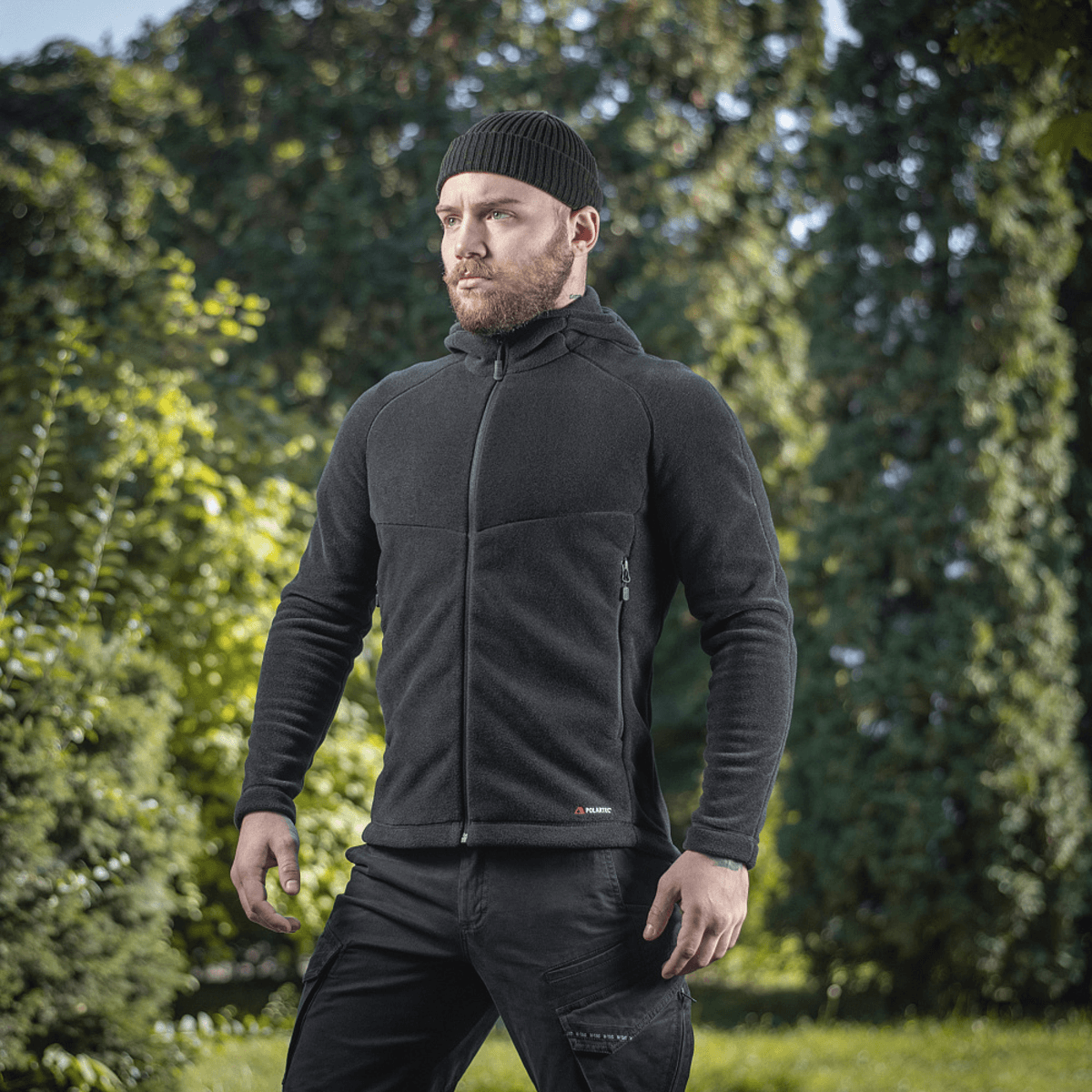 Mand iført M-Tac Sprint Fleece Sweatshirt Polartec i sort i frodigt skovmiljø, fremhæver stilfuld funktionalitet og komfort.