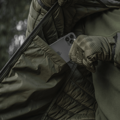 Person iført M-Tac Stalker Gen.III Jakke med smartphone i lomme, mens han justerer jakken, viser stil og funktionalitet.
