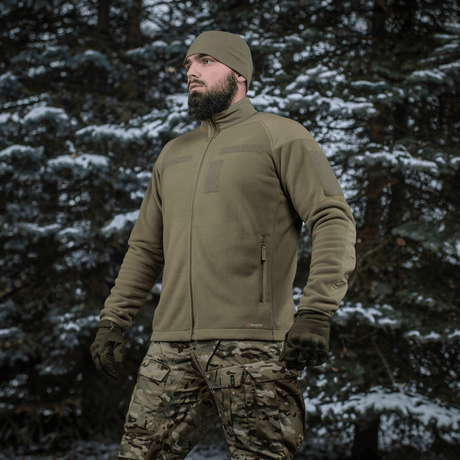 Mand iført M-Tac Combat Fleece Polartec Jakke i skovmiljø, viser jakken's funktionelle og taktiske design, ideel til udendørs brug.