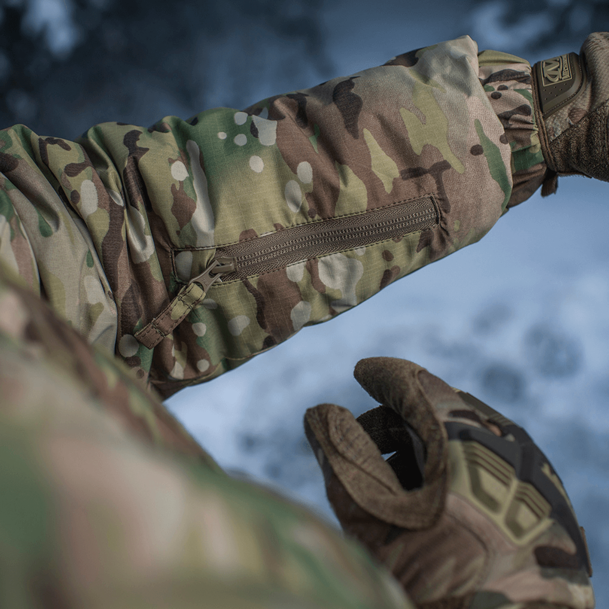 Detalje af M-Tac Alpha Gen.IV Pro Primaloft Vinterjakke med Multicam mønster, viser lynlåslomme og vandafvisende materiale.