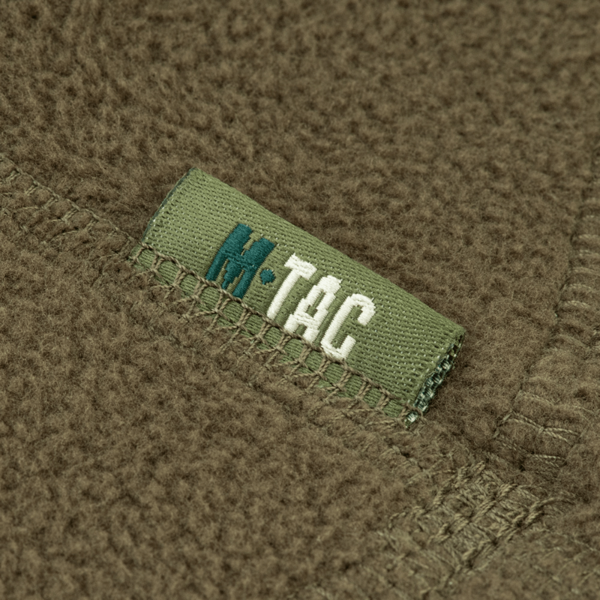 Nærbillede af M-Tac Anatomisk Snood Justerbar Elite Fleece (320 g/m²) med synlige stofdetaljer og logo på grøn baggrund.