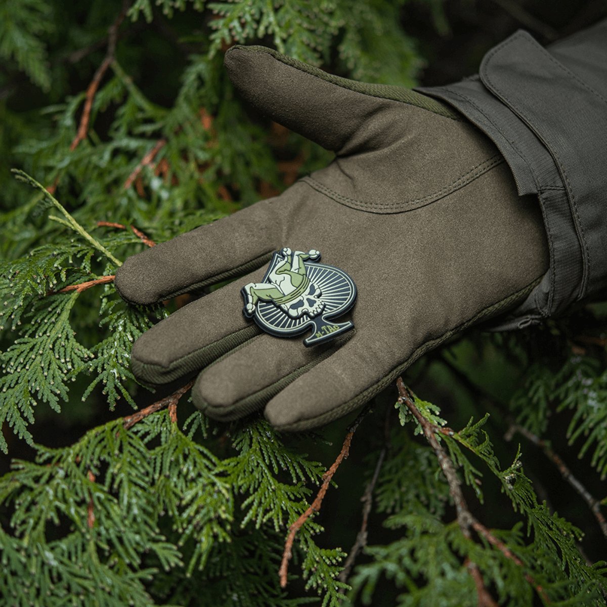 M-Tac Ace of Spades 3D PVC Patch i gloved hand, på en baggrund af grene