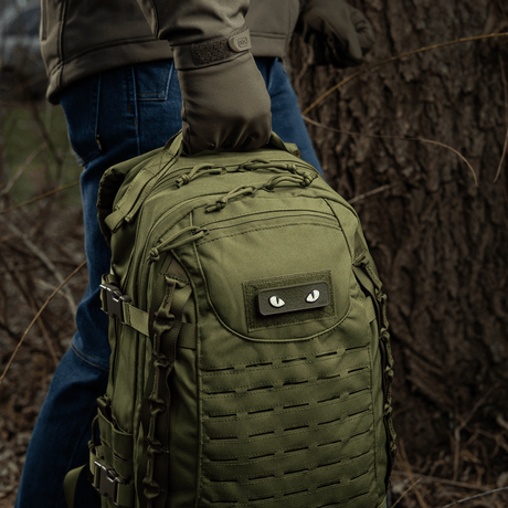 M-Tac Cat Eyes 3D PVC Patch on backpack in forest, ideal for tactical and outdoor activities, reflective design, easy attachment with Velcro.