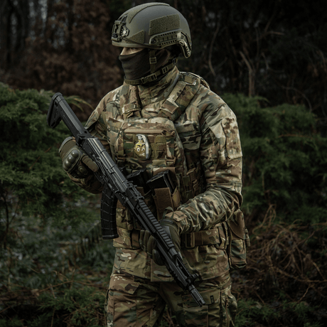 A soldier in camouflage with an M-Tac Patch M67 Grenade 3D PVC on his vest, equipped with tactical gear in a forest setting.