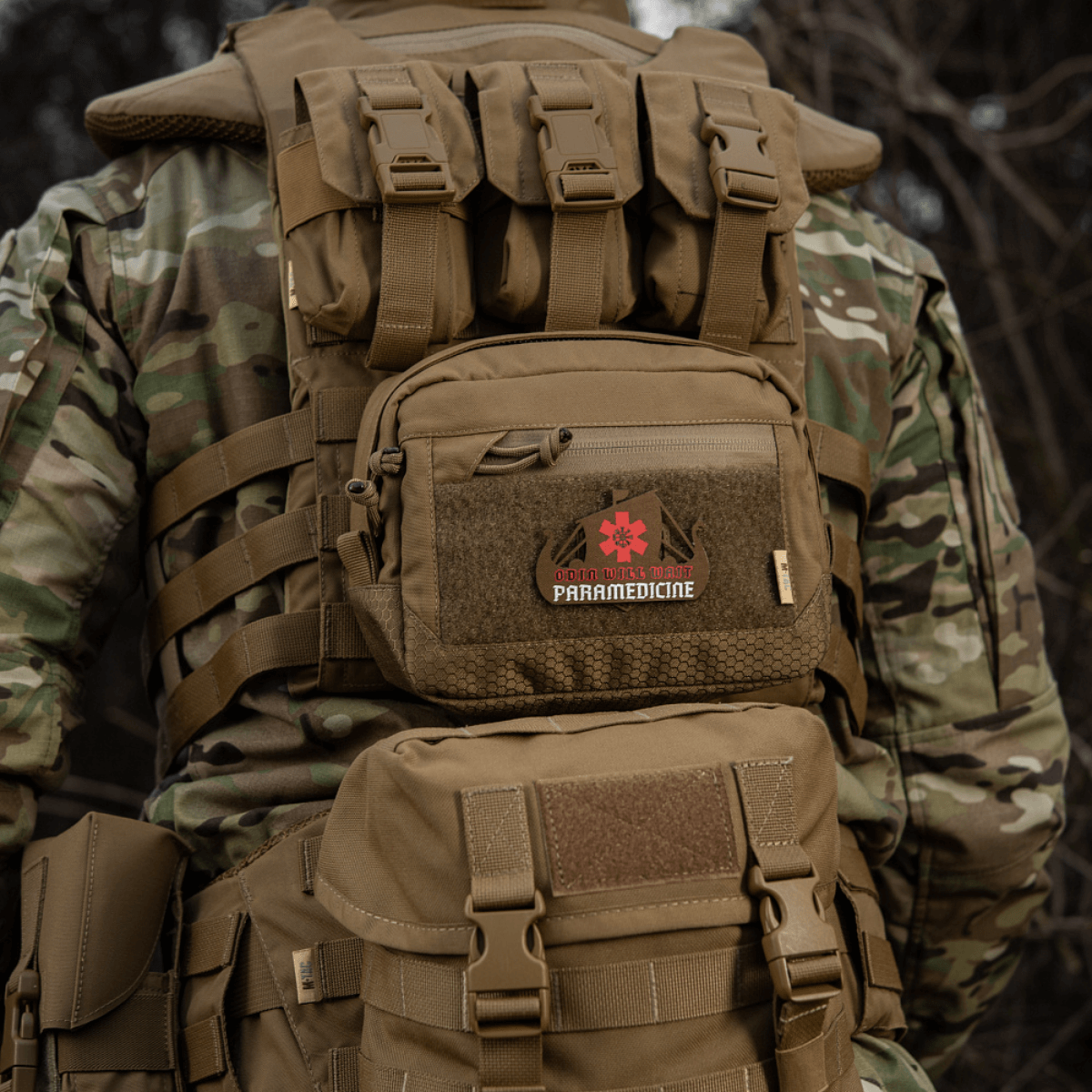 Taktisk rygsæk med 'Paramedicine' patch i camouflagemønster set bagfra i naturen, robust og holdbar til udendørs brug