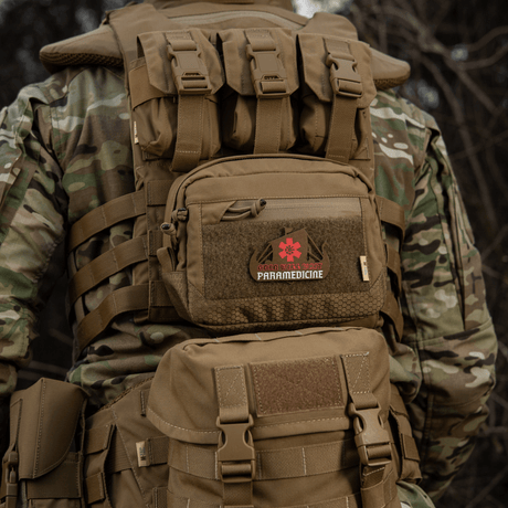 Tactical backpack with 'Paramedicine' patch in camouflage pattern seen from behind in nature, suitable for outdoor use.