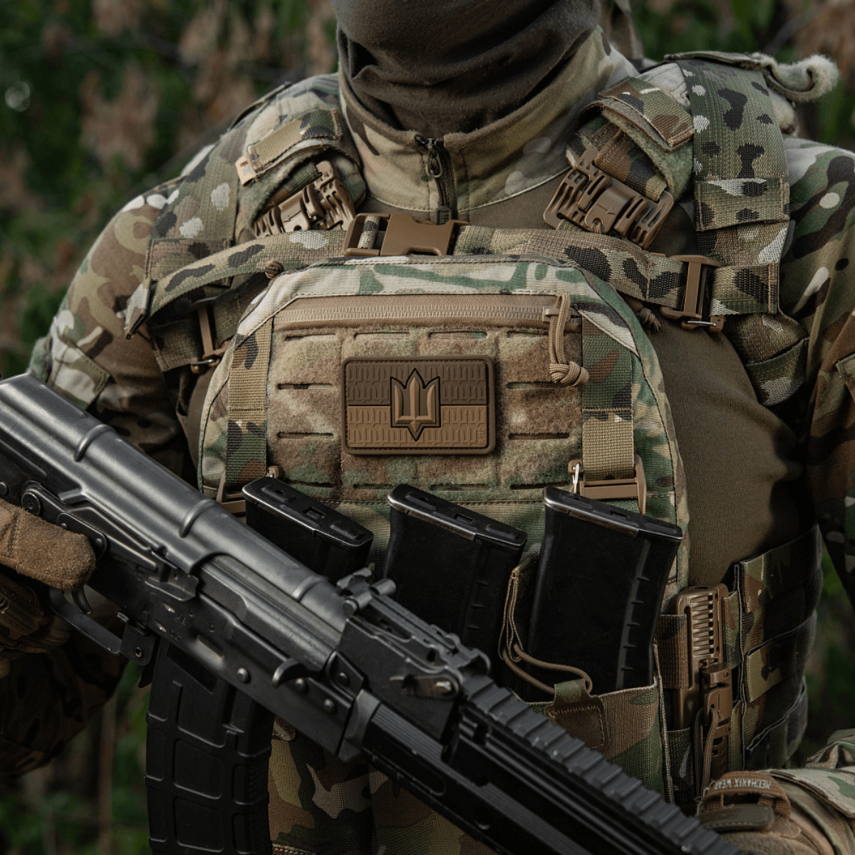Soldat iført camouflagevest med M-Tac patch Ukraine Flag med ZSU Trident PVC, og holder gevær, symboliserer ukrainsk stolthed og arv.