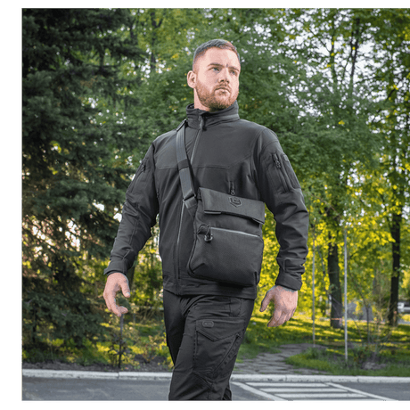 Man wearing M-Tac Konvert Taske Elite outdoors in a park, dressed in black and walking in natural light, showing the bag's comfort and style.