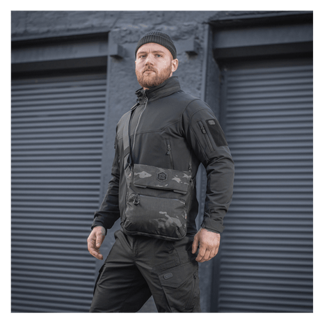 Man wearing M-Tac Konvert Bag Elite in black camouflage style in front of industrial garage doors.